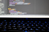 Close-up of hands coding on a computer keyboard with colorful code on screen