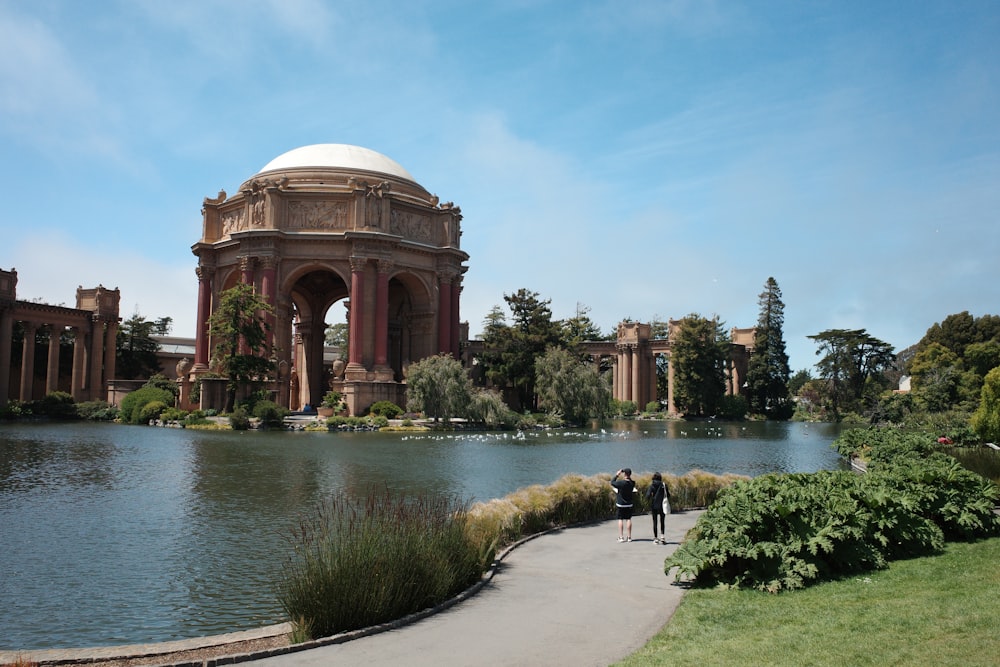 a couple people walking by a river with Palace of Fine Arts in the background