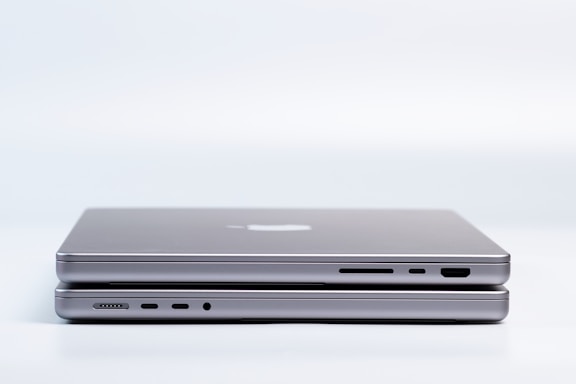 Two sleek, modern laptops are placed on top of each other, highlighting the slim design and metallic finish. Various ports are visible on the side, emphasizing the functionality and technology.