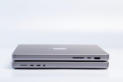 Two sleek, modern laptops are placed on top of each other, highlighting the slim design and metallic finish. Various ports are visible on the side, emphasizing the functionality and technology.