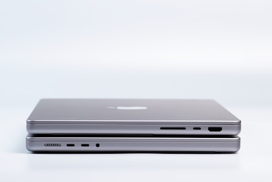 Two sleek, modern laptops are placed on top of each other, highlighting the slim design and metallic finish. Various ports are visible on the side, emphasizing the functionality and technology.