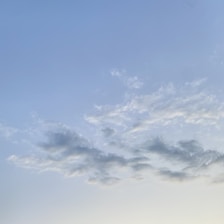 Light and wispy clouds scattered across a vast blue sky with a gradient transitioning from blue to a lighter shade towards the horizon.