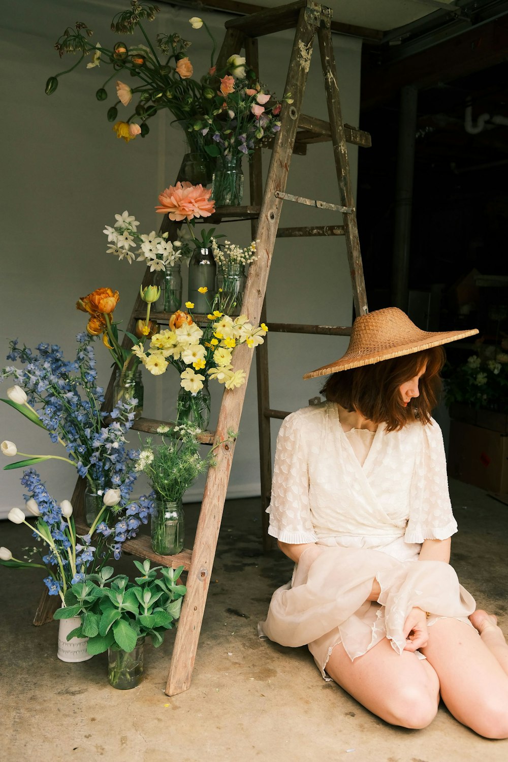 a girl sitting on the ground next to a vase of flowers