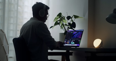 A person using a headset while working on a laptop in a bright home office.