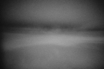 A grayscale image with a gradient effect, creating a hazy or misty appearance. The top section is darker, transitioning to lighter shades towards the bottom, giving a foggy or blurred impression.