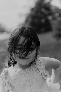 A charming child wearing a dark green velvet dress with gold accents, smiling softly in a sunlit boutique setting.