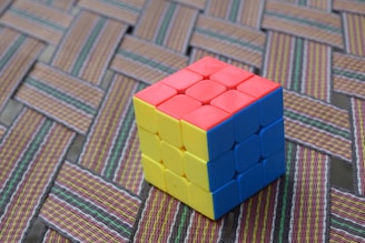 A multicolored Rubik's Cube is placed on a woven mat with intricate patterns and a mix of colors.