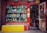 A vibrant storefront showcasing an array of decorative items and antiques, including colorful ceramic vases, figurines, and sculptures. The shop has a red frame around the window and door, with various traditional ornaments hanging from the door. The interior appears densely packed with more collectibles and curiosities.