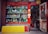 A vibrant storefront showcasing an array of decorative items and antiques, including colorful ceramic vases, figurines, and sculptures. The shop has a red frame around the window and door, with various traditional ornaments hanging from the door. The interior appears densely packed with more collectibles and curiosities.