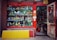 A vibrant storefront showcasing an array of decorative items and antiques, including colorful ceramic vases, figurines, and sculptures. The shop has a red frame around the window and door, with various traditional ornaments hanging from the door. The interior appears densely packed with more collectibles and curiosities.