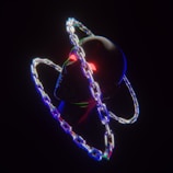 A dark, surreal image featuring a metallic humanoid head with glowing red eyes. It is encircled by two overlapping, luminous chains creating a halo effect. The chains emit multicolored light, casting a reflection on the head, and the overall scene is set against a black background.