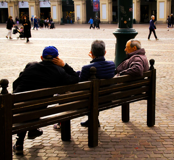 A candid moment of Peer chatting warmly with elderly citizens in a sunny town square.