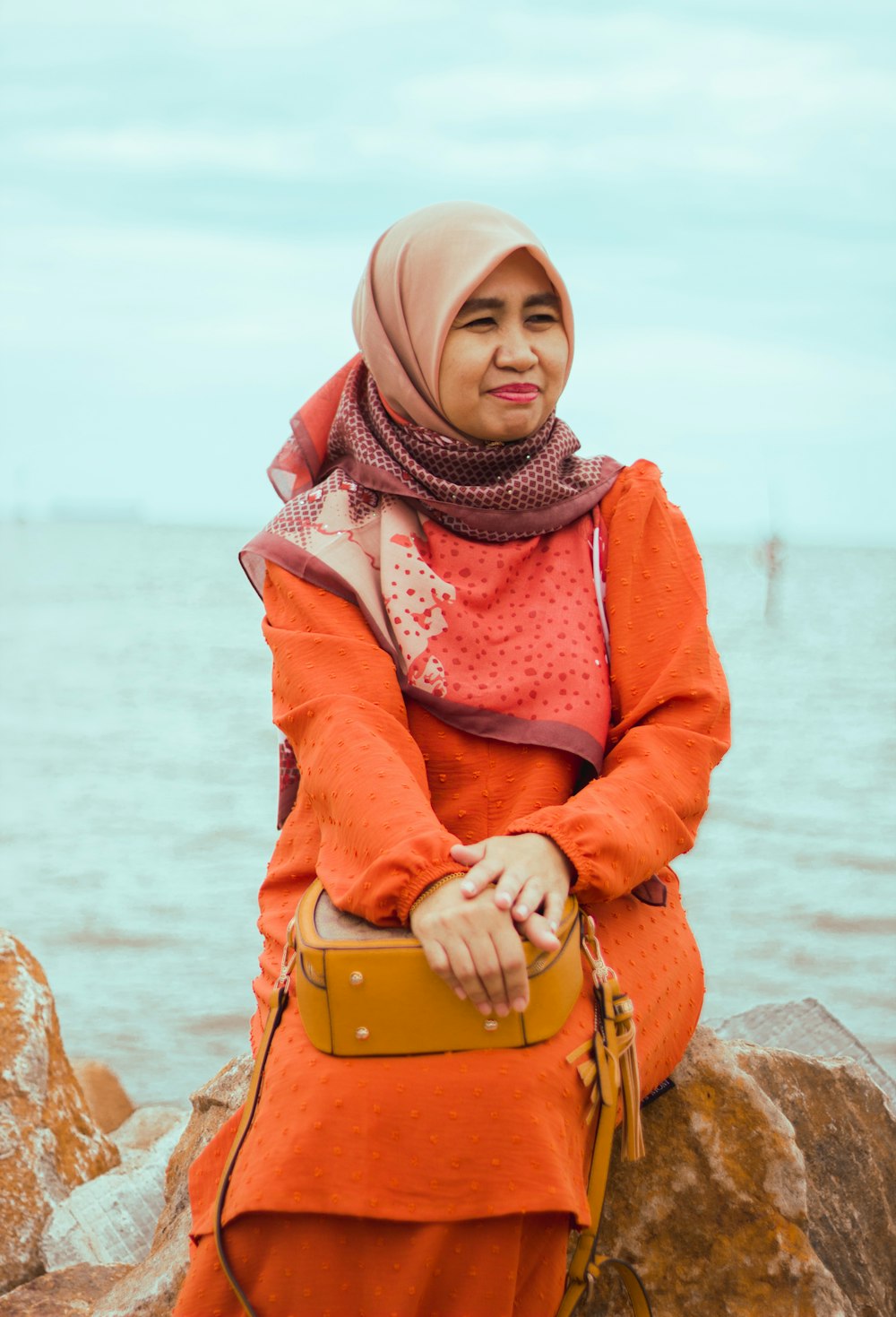 a person in a red coat sitting on a rock by the water