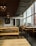 The image depicts an empty restaurant with minimalistic wooden furniture and a wall decorated with white and black doodles. The ceiling has multiple lantern-style light fixtures, and large windows on one side allow ample daylight to stream in. A blackboard on one of the walls reads 'Asian Street Food' and displays several menu items. The overall ambiance is modern and relaxed.