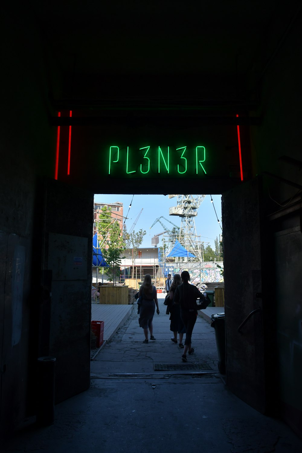a group of people walking down a sidewalk with a neon sign above them