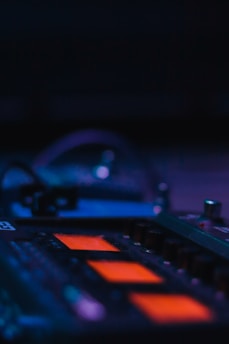 A close-up of electronic music equipment with colorful lights glowing in a dark studio.