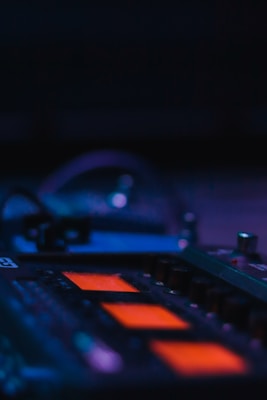 A close-up of a piece of audio equipment with glowing orange screens and various knobs and dials. The background is dark, creating a contrast with the illuminated details of the device, suggesting a studio or performance setting.