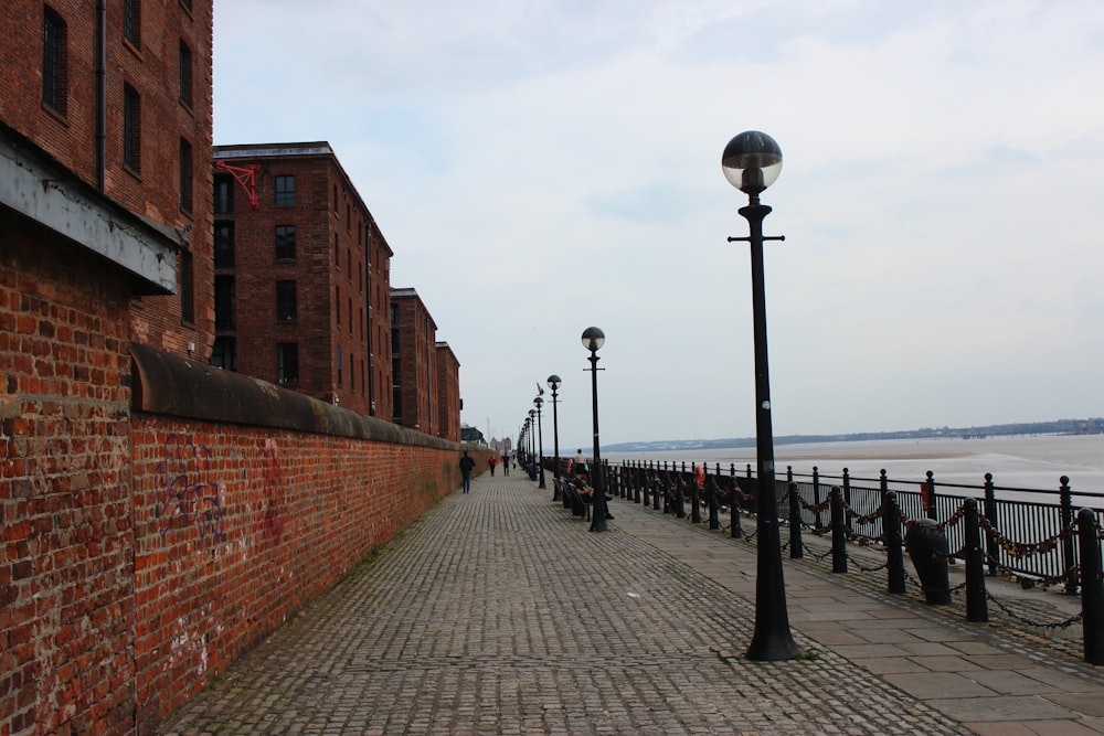 a brick walkway with a lamp post and a brick wall and a body of water