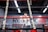 A person is training inside a boxing ring, with 'Everlast' branding visible on the ropes. The focus seems to be on the foreground ropes, while the person appears slightly blurred in the background. The setting includes a gym-like environment with dim lighting and industrial design elements.