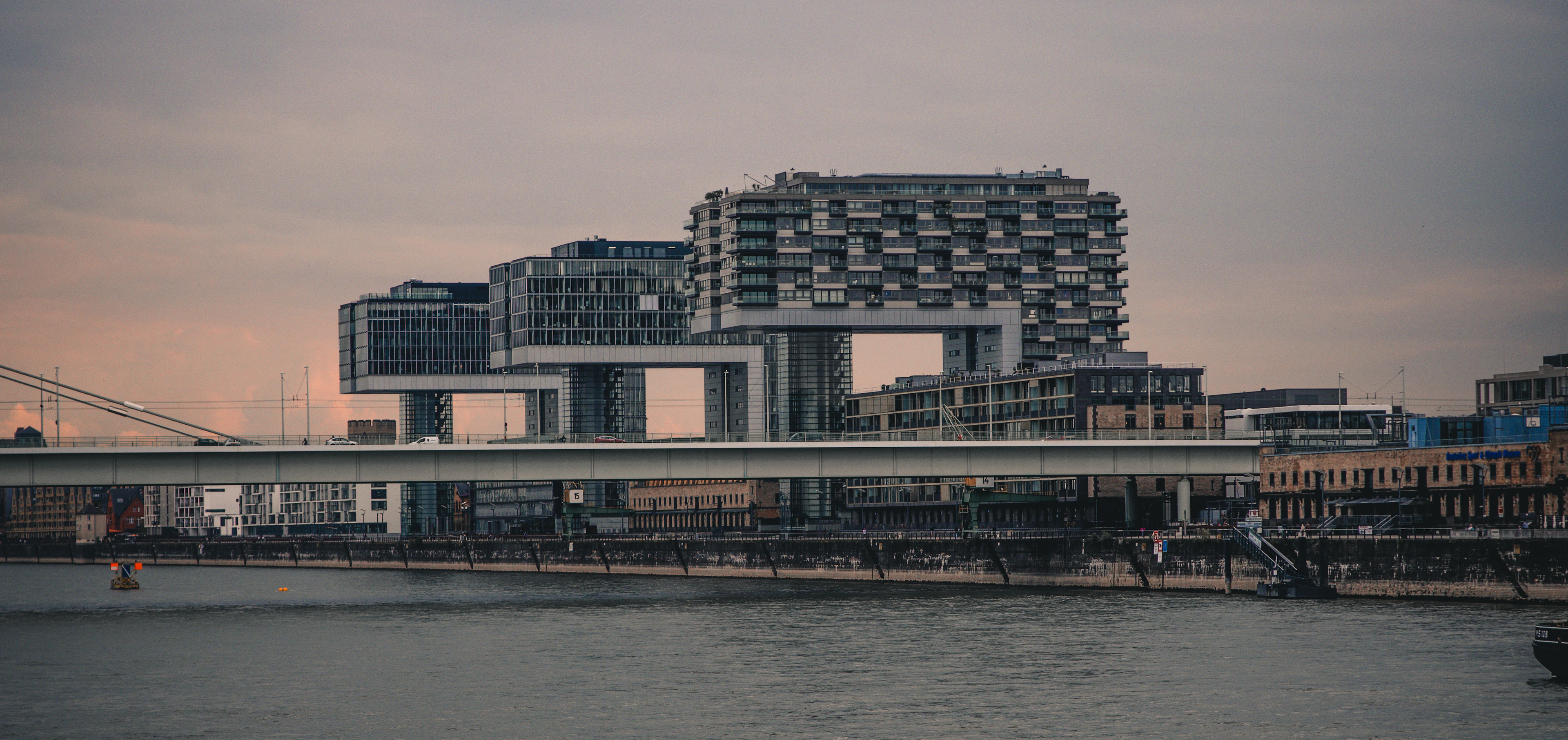 Cologne's crane-shaped Kranhaus buildings glow above the Rhine harbor at dusk, reflected in the water.