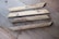 Four wooden planks are lying on a wooden floor. The planks have a natural, rustic finish, and two of them have screws partially embedded. The floor has a variegated pattern with a mix of light and dark brown tones.