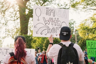 A compassionate woman holding a support sign in a peaceful park setting.