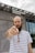 A person with a striped shirt and braided beard stands in front of a modern building with a sign that reads Hewlett Packard Enterprise. The person is pointing directly at the camera with a focused expression.