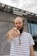A person with a striped shirt and braided beard stands in front of a modern building with a sign that reads Hewlett Packard Enterprise. The person is pointing directly at the camera with a focused expression.