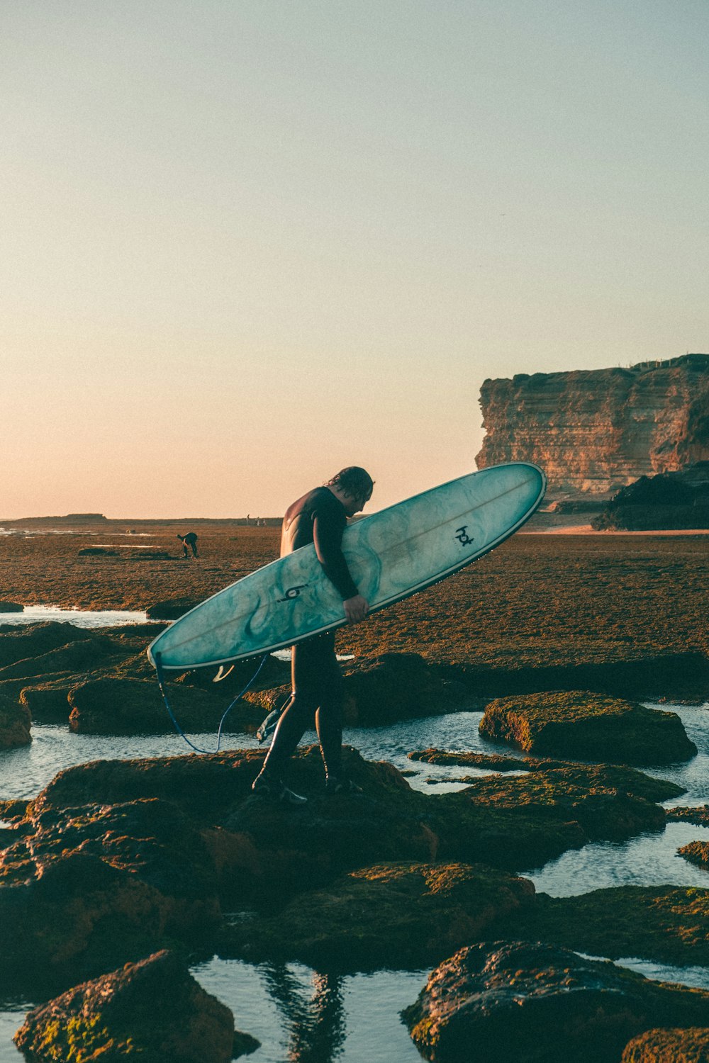 a person carrying a surfboard on a rocky beach