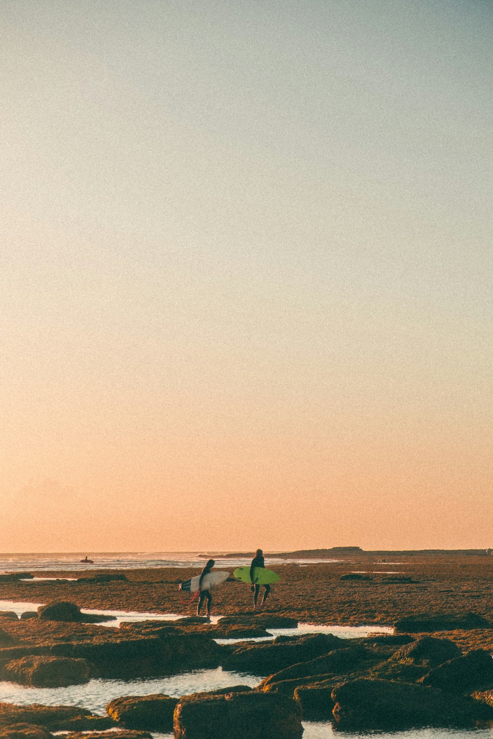 a group of people walk on a beach carrying surfboards