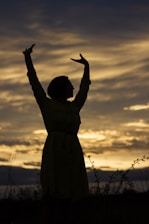An inspiring outdoor scene of a person standing confidently with arms raised against a sunrise backdrop.