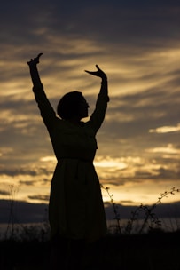 An inspiring outdoor scene of a person standing confidently with arms raised against a sunrise backdrop.