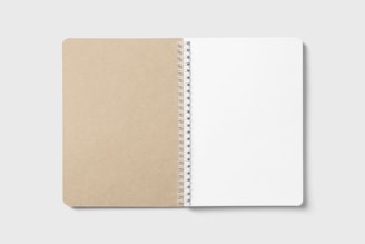 An open spiral-bound notebook on a plain background, with a brown cardboard cover on the left and blank white pages on the right.