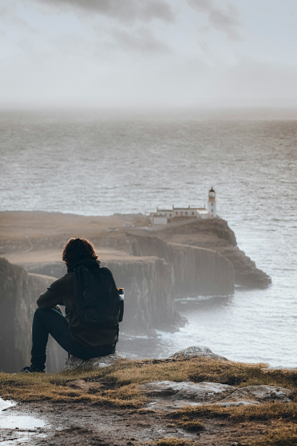 Una persona sentada en una roca mirando un faro