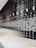 A modern interior space with a large reflective wall and an array of lights hanging from the ceiling. The wall features a series of horizontal patterns, and the reflection creates a distorted visual effect. The floor is polished and shiny, adding to the sleek design.
