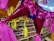 Brightly colored piñatas with shiny pink wrapping and yellow tassels are hanging indoors against the backdrop of a grocery store. Numerous shelves are filled with assorted products including jars and cans organized neatly.