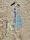 UV bracelet in aqua and tan colors resting on a beach towel with seashells nearby under bright sunlight