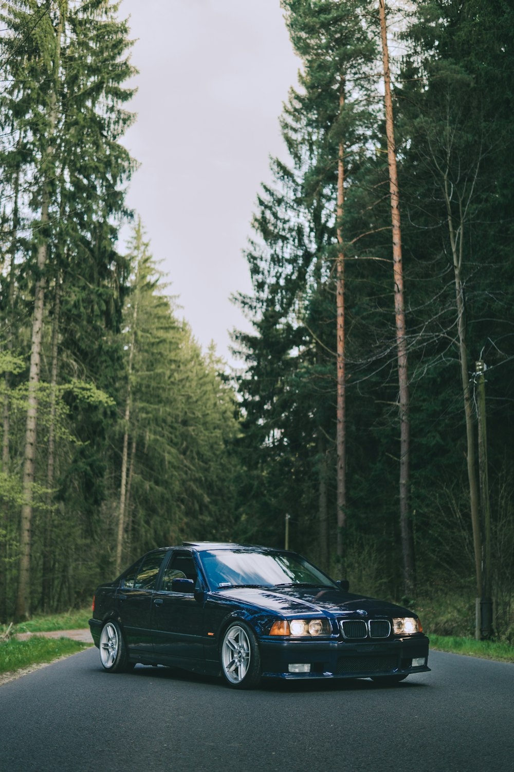 a black car parked on a road with trees on either side