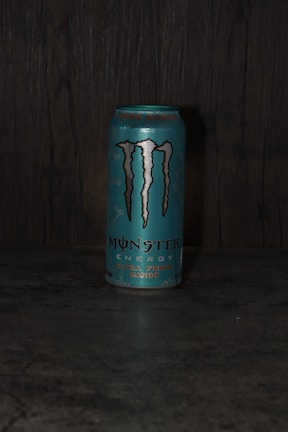 A can of Monster Energy drink, specifically the 'Ultra Fiesta Mango' flavor, is placed on a dark surface. The can is primarily blue with the iconic Monster logo in black and silver. The background appears to be a textured dark material, possibly wood or stone.