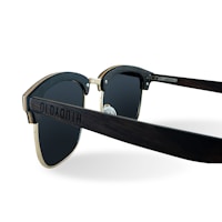 A pair of stylish sunglasses with dark lenses and a wooden frame. The arms have a slightly curved design and the frame includes metallic accents. The sunglasses display intricate detailing on the side, giving a modern and chic appearance.