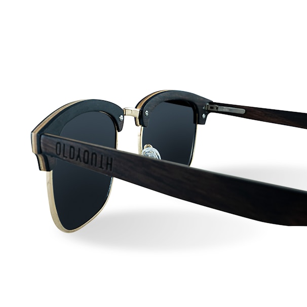 A pair of stylish sunglasses with dark lenses and a wooden frame. The arms have a slightly curved design and the frame includes metallic accents. The sunglasses display intricate detailing on the side, giving a modern and chic appearance.