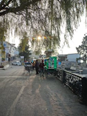a group of people walking down a street with a cart and a tree