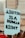 A sign being held at a protest that reads 'Abortion is a Human Right' in bold, black letters on a light blue background. The sign is in focus, while the background appears to be a blurred crowd and a building.