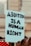 A sign being held at a protest that reads 'Abortion is a Human Right' in bold, black letters on a light blue background. The sign is in focus, while the background appears to be a blurred crowd and a building.