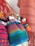 A collection of handmade dolls adorned in colorful, traditional woven garments, featuring vibrant patterns. The dolls have bright hats and distinct facial features, with backgrounds of similar textile material.