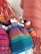 A collection of handmade dolls adorned in colorful, traditional woven garments, featuring vibrant patterns. The dolls have bright hats and distinct facial features, with backgrounds of similar textile material.