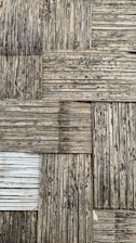 A textured surface consisting of interwoven bamboo strips arranged in a square pattern. The bamboo appears weathered, with a mix of dark and light brown shades, and some areas show signs of aging or wear.