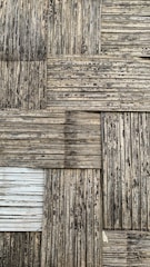 A textured surface consisting of interwoven bamboo strips arranged in a square pattern. The bamboo appears weathered, with a mix of dark and light brown shades, and some areas show signs of aging or wear.
