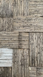 A textured surface consisting of interwoven bamboo strips arranged in a square pattern. The bamboo appears weathered, with a mix of dark and light brown shades, and some areas show signs of aging or wear.