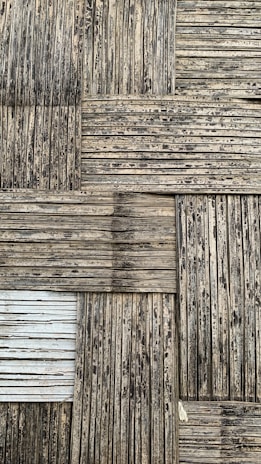 A textured surface consisting of interwoven bamboo strips arranged in a square pattern. The bamboo appears weathered, with a mix of dark and light brown shades, and some areas show signs of aging or wear.